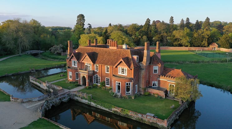 Boxted Hall, Suffolk – Red brick country house with tall chimneys beside moat and bridge.