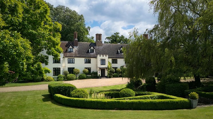 Hill House Norfolk, Norfolk – Cream-rendered country house with black gable windows, brick chimneys, gravel drive, and manicured grounds with topiary hedges.