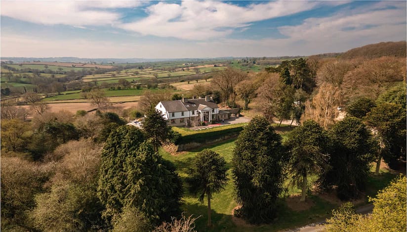 Holly House, Derbyshire – Aerial view of country house with ivy-covered trees and rolling valley farmland beyond.