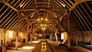 The Tudor Barn, Suffolk – Historic timber-frame barn interior with exposed oak beams and brick walls, lit by uplighting.