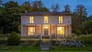 Henge Estate, Wiltshire – Two-storey rendered country house with columned veranda and illuminated windows at dusk.
